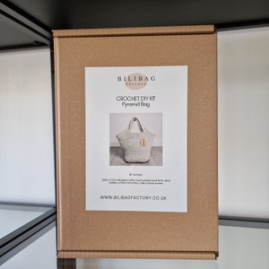 May include: A brown cardboard box with a white label that says "BILIBAG Factory" and "CROCHET DIY KIT Pyramid Bag". The label also shows a picture of a white crocheted bag and the text "Kit contains 200m of 5mm Braided Cotton Cord, crochet hook, hook size, stitch marker, written instructions, video tutorial and access. WWW.BILIBAGFACTORY.CO.UK"
