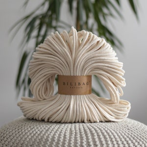 May include: A close-up of a large spool of natural cotton rope, wrapped around a brown label that reads "Bilibag Factory".
