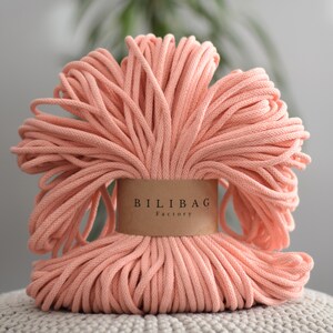 May include: A close-up of a large bundle of peach-coloured cotton rope. The rope is wrapped around a brown label that reads "Bilibag Factory".