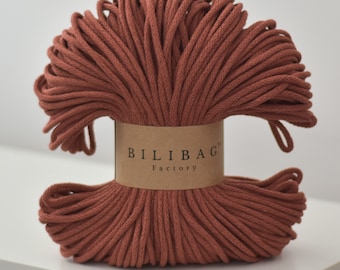 May include: A roll of terracotta-colored cotton cord, wrapped around a brown paper label that reads "Bilibag Factory".
