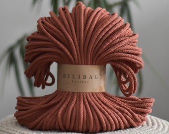 May include: A spool of terracotta-colored macrame cord. The cord is tightly wound and secured with a brown paper band that reads "BILIBAG Factory". The cord is a warm, earthy tone, suitable for various crafting projects.