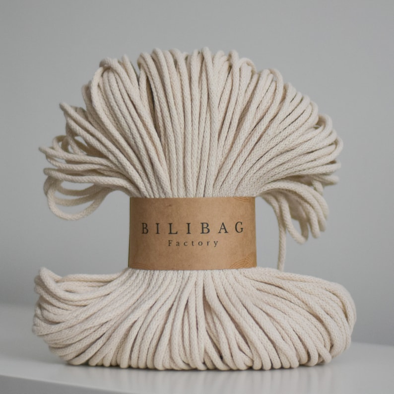 Op de afbeelding: Een close-up van een grote spoel natuurlijke katoenen touw, gewikkeld in een bruin papieren label met de tekst "Bilibag Factory".