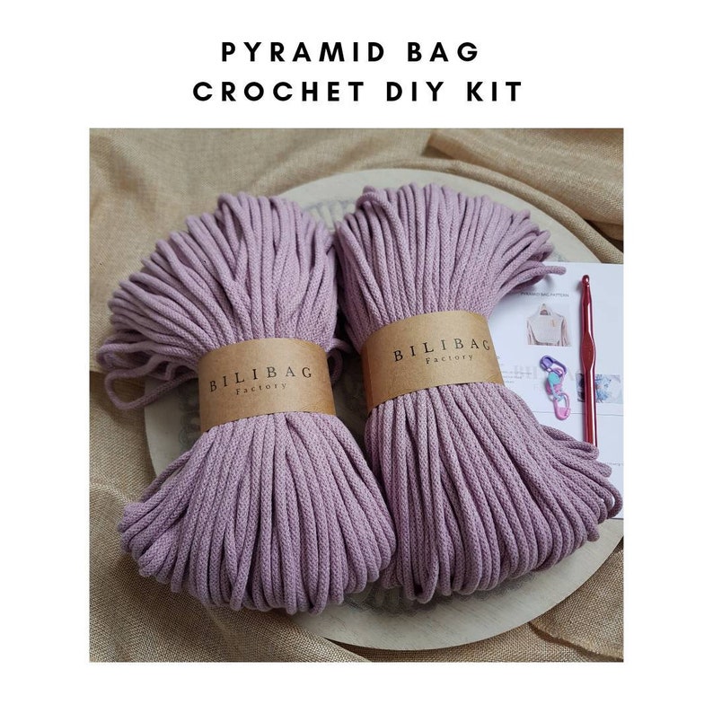 May include: A crochet DIY kit for making a pyramid bag. The kit includes two balls of purple cotton cord, a crochet hook, and a set of instructions. The cord is labeled "Bilibag Factory".