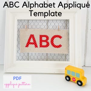May include: A white framed sign with the letters "ABC" in red polka dot fabric. The sign is hanging in front of chicken wire. A yellow school bus toy is in the foreground. The text "ABC Alphabet Appliqué Template" is at the top.