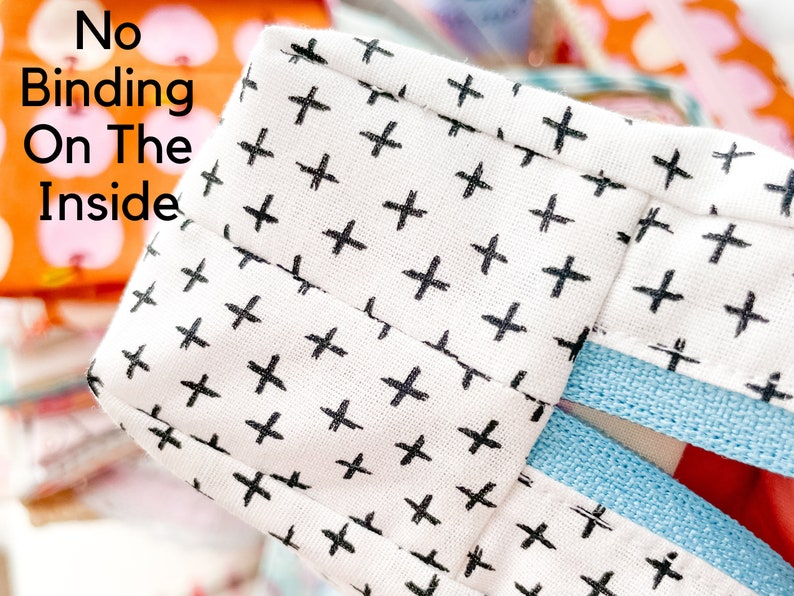 May include: Close-up of a white fabric with a black cross pattern. The text "No Binding On The Inside" is visible. A light blue fabric edge is also visible, along with a glimpse of a colorful pattern in the background.
