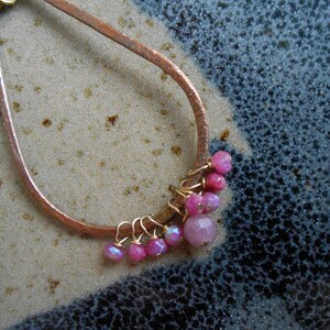 May include: A copper wire hoop with a cluster of pink and iridescent gemstone beads hanging from it.