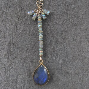 May include: A gold chain necklace with a teardrop-shaped blue labradorite gemstone pendant. The chain is adorned with iridescent beads.
