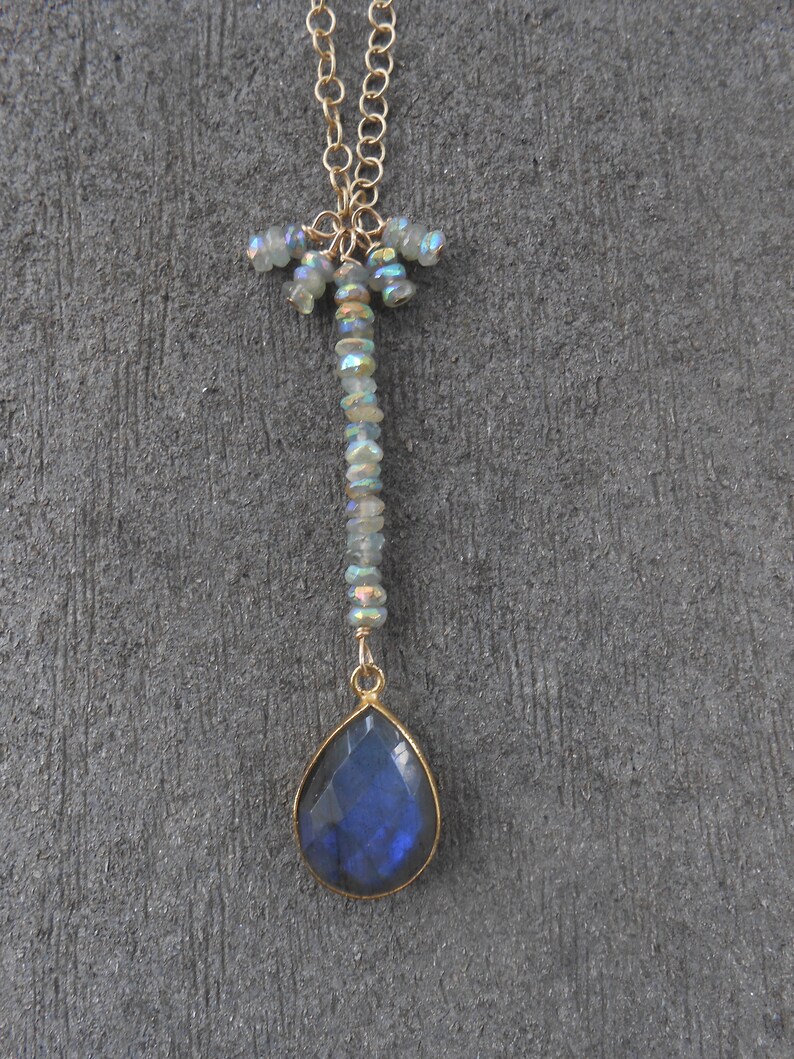 May include: A gold chain necklace with a teardrop-shaped blue labradorite gemstone pendant. The chain is adorned with iridescent beads.