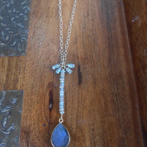 May include: A gold chain necklace with a teardrop-shaped blue gemstone pendant and a cluster of iridescent beads at the top.