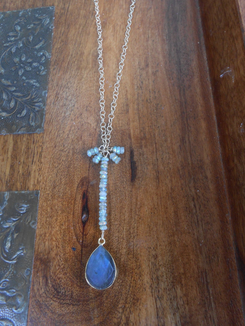 May include: A gold chain necklace with a teardrop-shaped blue gemstone pendant and a cluster of iridescent beads at the top.