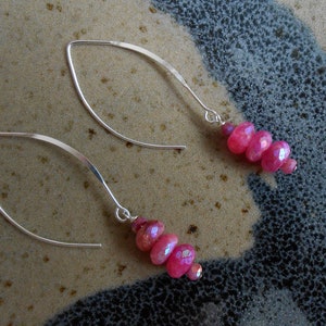 May include: A pair of silver dangle earrings with pink faceted gemstone beads. The earrings have a simple, elegant design.