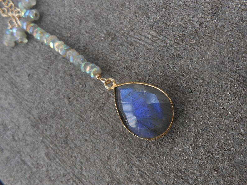 May include: A gold necklace featuring a teardrop-shaped blue labradorite gemstone pendant and a chain of iridescent beads.