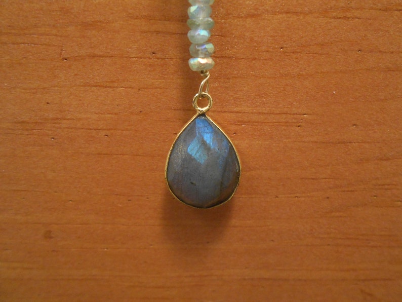 May include: A teardrop-shaped pendant with a blue iridescent gemstone, hanging from a silver chain.