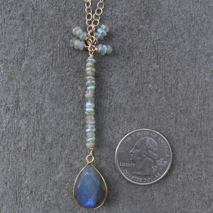 May include: A gold chain necklace with a dragonfly pendant made of iridescent blue and green stones. The pendant is attached to a teardrop-shaped blue labradorite gemstone.