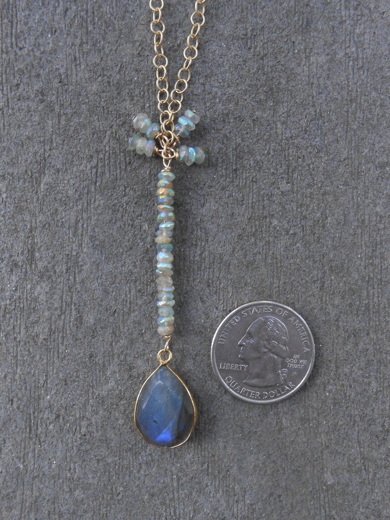May include: A gold chain necklace with a dragonfly pendant made of iridescent blue and green stones. The pendant is attached to a teardrop-shaped blue labradorite gemstone.