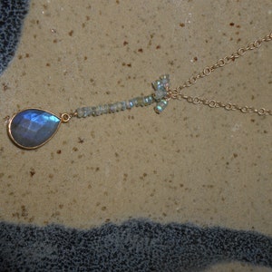 May include: A gold chain necklace with a teardrop-shaped blue gemstone pendant and a cluster of smaller iridescent gemstones.