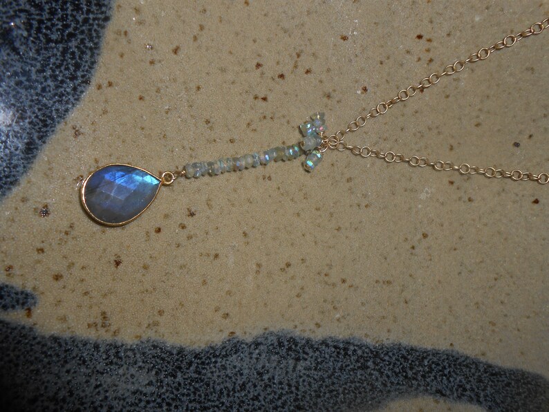 May include: A gold chain necklace with a teardrop-shaped blue gemstone pendant and a cluster of smaller iridescent gemstones.