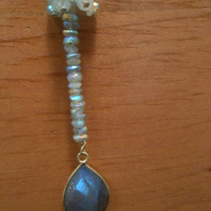 May include: A teardrop-shaped pendant necklace with a blue iridescent stone and a chain of iridescent beads.