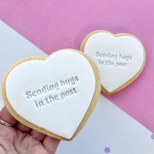May include: Two heart-shaped sugar cookies with white icing and the text "Sending hugs in the post" on each cookie.