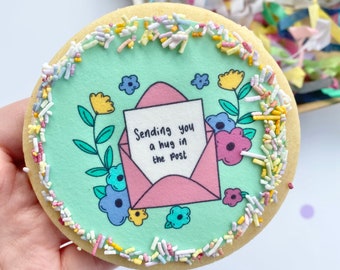 May include: A light green cookie decorated with colorful sprinkles and a pink envelope with the text "Sending you a hug in the post".