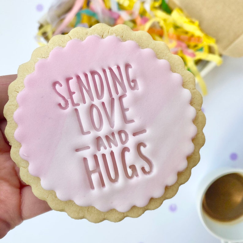 May include: A pink and white iced cookie with the text "Sending Love - and - Hugs" in white icing.