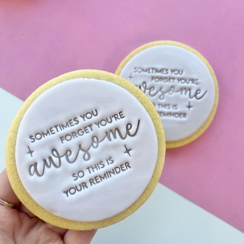 May include: Two round sugar cookies with white icing and a silver message that reads "Sometimes you forget you're awesome so this is your reminder".