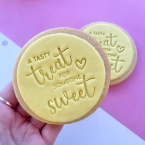 May include: Two yellow sugar cookies with a white icing design. The icing says "A tasty treat for someone sweet" with a heart symbol.