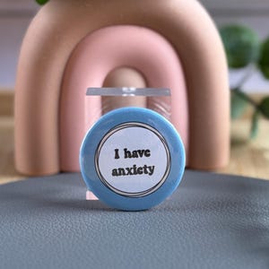 May include: A blue button with white text that reads "I have anxiety". The button is sitting on a grey surface.