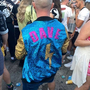 May include: A blue sequined jacket with gold sequins on the sleeves. The jacket has a pink lightning bolt and the name "DAVE" written on the back.