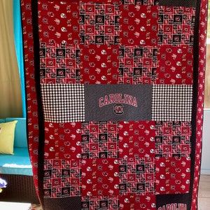 May include: A red, black, and white patchwork quilt with a University of South Carolina logo and the names "Brooke" and "B.J.N." embroidered on it.