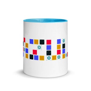 Pode incluir: Caneca de cerâmica branca com uma borda azul claro. A caneca apresenta um design geométrico colorido com quadrados e estrelas em tons de vermelho, azul, amarelo, preto e verde.