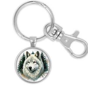 May include: Silver-toned keychain with a round pendant featuring a detailed illustration of a white wolf against a backdrop of evergreen trees. The keychain includes a large split keyring and a swivel snap hook. The text on the image says: keychain with large split keyring & swivel snap hook.