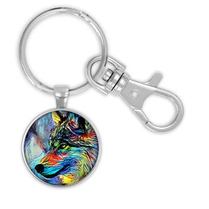 May include: Silver keychain with a round pendant featuring a colorful wolf portrait. The keychain includes a large split keyring and a swivel snap hook. The wolf design showcases vibrant hues of blue, yellow, red, and green.