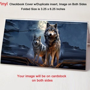 May include: A checkbook cover with a vinyl finish featuring a nighttime scene with two wolves standing in front of a full moon. The cover is 3.25 inches by 6.25 inches and has a duplicate insert. The text "Your image will be on cardstock on both sides" is printed on the bottom of the cover.