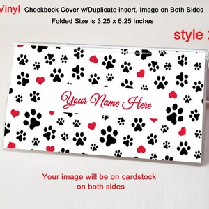 May include: A vinyl checkbook cover with a paw print and heart pattern. The cover is white with black paw prints and red hearts. The text "Your Name Here" is in a script font. Folded size is 3.25 x 6.25 inches.