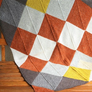 May include: A knitted blanket with a geometric pattern in shades of gray, white, orange, and yellow.