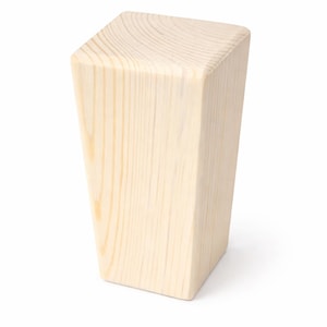 May include: A light-colored, wooden furniture leg with a trapezoidal shape. The leg is made of light-colored wood with visible grain and a smooth finish. The top is a flat, rectangular surface.