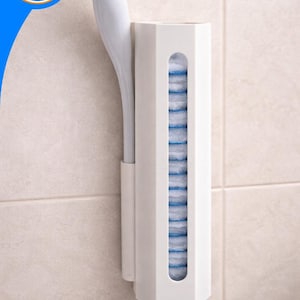 Op de afbeelding: Een witte wandhouder voor de badkamer met een verticale gleuf die een stapel blauwe en witte wegwerp-toiletpads bevat, met een apart zijvak voor een witte toiletborstel met een lange steel.