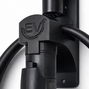 Puede incluir: Soporte negro para cargador de vehículo eléctrico fijado a una pared blanca. Presenta el texto "EV" con un diseño de hoja. El logotipo "C3D PRINTS" es visible en la esquina superior izquierda.