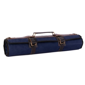 May include: A blue canvas roll-up bag with brown leather straps and brass buckles. The bag has a handle and is designed to hold and protect knives.
