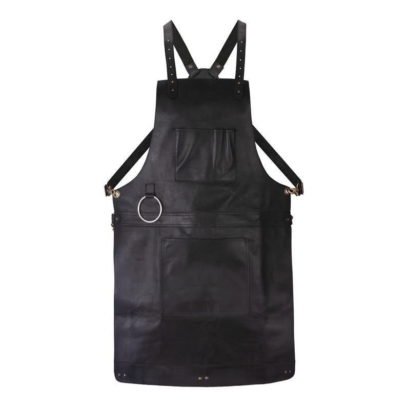 May include: A black apron featuring adjustable shoulder straps with metal buckles, a chest pocket, a large lower pocket, and a silver-toned metal ring attached to the side. The apron is constructed with reinforced stitching and metal rivets.