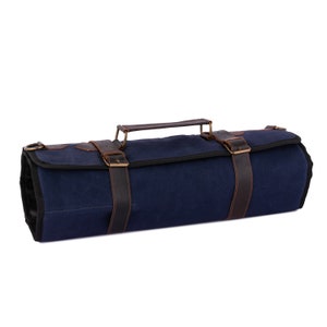 May include: A blue canvas roll-up bag with brown leather straps and a handle. The bag is closed and has a flap with a buckle.