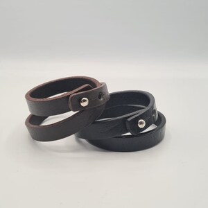 May include: Two leather bracelets, one brown and one black, with silver metal accents. The bracelets are wrapped around each other.
