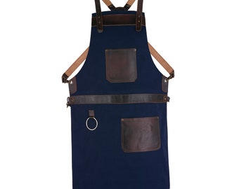 Può includere: Un grembiule in tela blu navy con cinturini e tasche in pelle marrone. Il grembiule ha un anello di metallo sul davanti e una grande tasca sul fondo.
