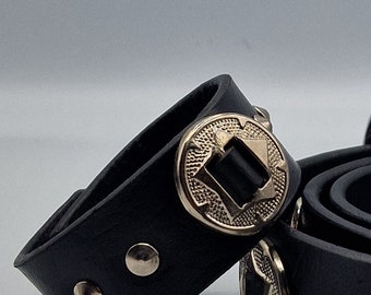 May include: Two black leather bracelets with silver metal accents. Each bracelet has a large, round, silver metal buckle with a square design in the center. The bracelets are adorned with small, round, silver metal studs.
