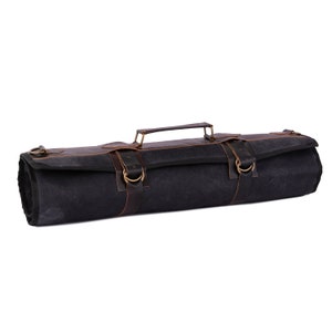 May include: A black canvas roll-up bag with brown leather straps and buckles. The bag has a brown leather handle and is designed to hold and protect knives.