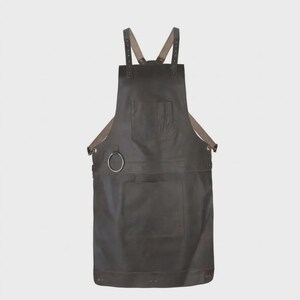 May include: A dark brown leather apron featuring adjustable shoulder straps with metal buckles, a chest pocket, a large lower pocket, and a circular metal ring attached to the side for hanging tools. The apron has a smooth, matte finish.