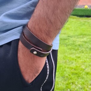 May include: A brown leather bracelet with a silver buckle. The bracelet is wrapped around a person's wrist.