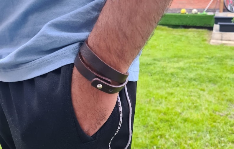May include: A brown leather bracelet with a silver buckle. The bracelet is wrapped around a person's wrist.