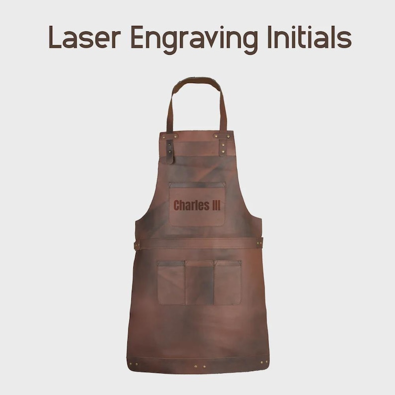 May include: A brown leather apron featuring a neck strap, a chest pocket with the laser-engraved text Charles III, and three lower pockets. The apron is secured with metal rivets at the strap attachment points and along the lower hem.